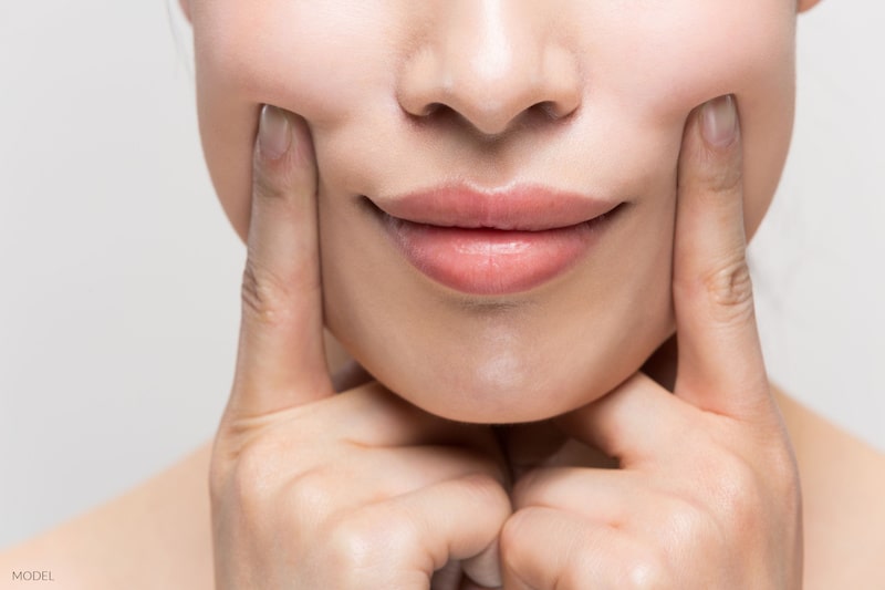 A woman pressing her fingers against her cheeks.