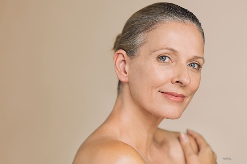 Beautiful older woman with grey hair in a bun looks at camera.