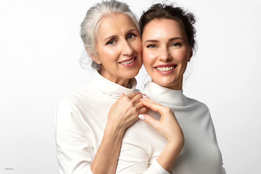 A younger and older woman, both wearing white, show off their beautiful skin.