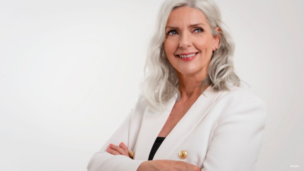 mature woman wearing a white blazer, black top, standing against a white background