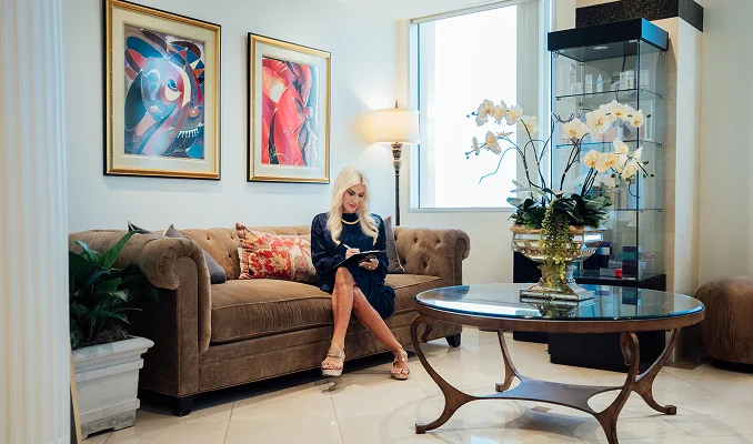 Woman sitting in elegant living room with brown sofa, colorful artwork, and glass coffee table