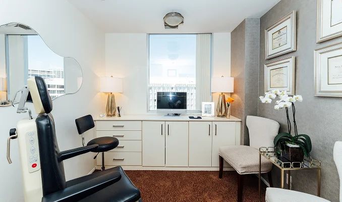 Modern home office with white built-in cabinets, black leather chair, window, and wood flooring