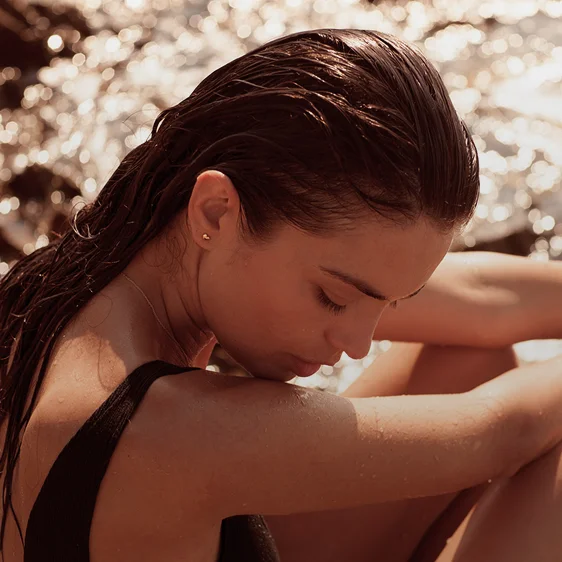 Woman with wet slicked-back hair in black swimsuit relaxing by water on sunny day - Injectables in Newport Beach, CA