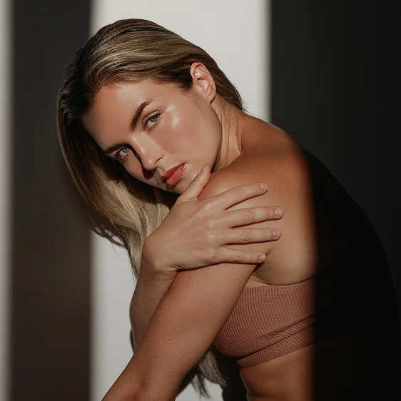 Woman with blonde hair in neutral toned off-shoulder top posing elegantly against white wall with dramatic lighting - Rhinoplasty in Newport Beach, CA