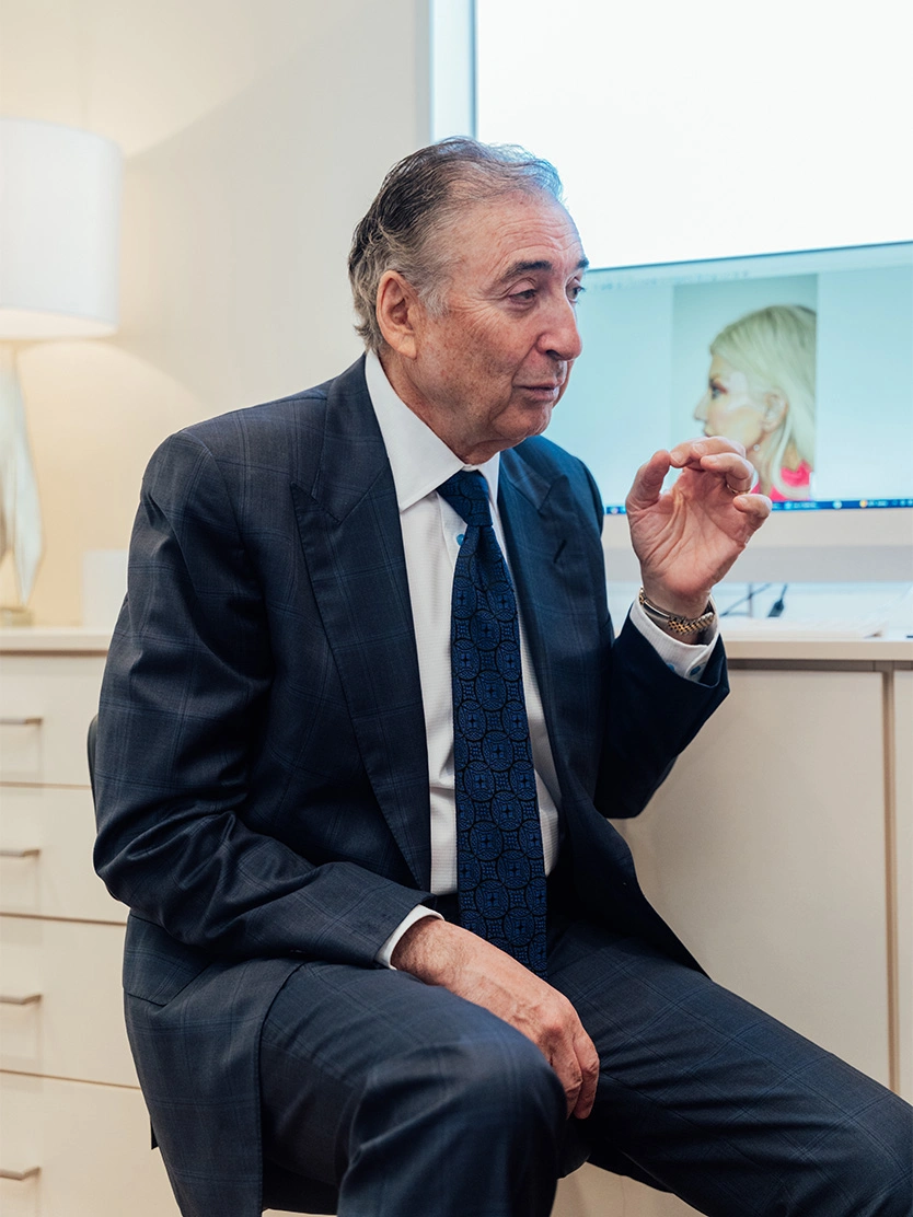 Boris M. Ackerman, MD in dark suit gesturing while speaking during presentation with display screen in background - Fat transfer in Newport Beach, CA
