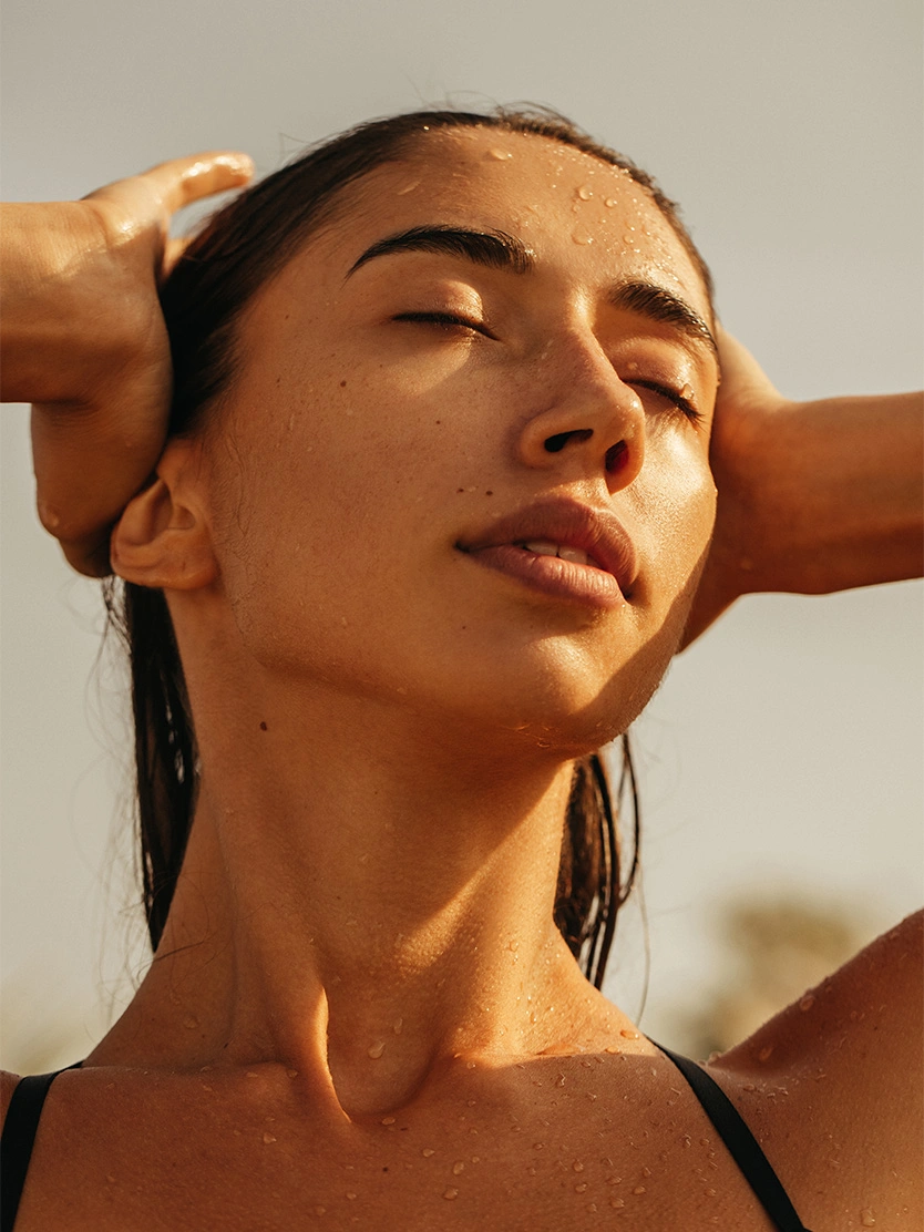Woman with slicked back wet hair and glowing skin in natural sunlight wearing gold hoop earrings - Laser skin resurfacing in Newport Beach, CA