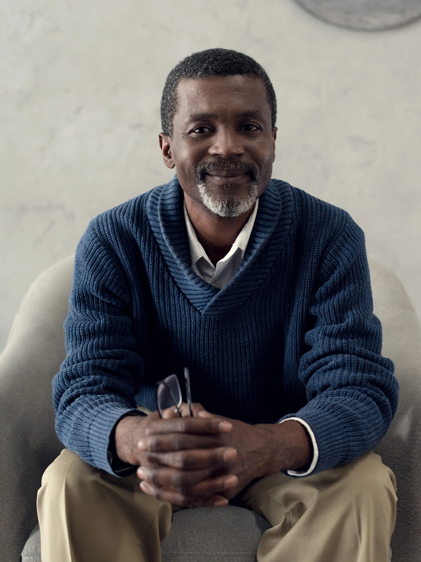 Smiling middle-aged man in blue sweater sitting with hands clasped in professional portrait - Male facelift in Newport Beach, CA