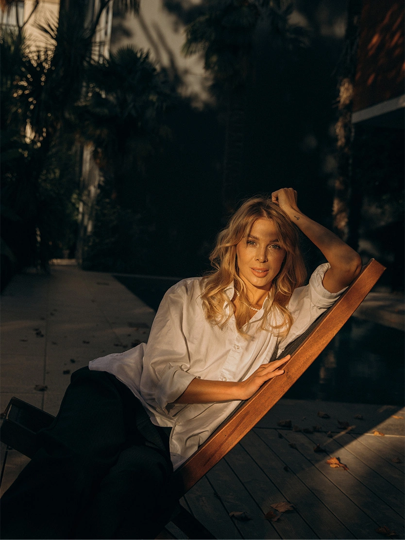 Woman relaxing in wooden deck chair outdoors during golden hour sunset wearing white shirt - Microneedling in Newport Beach, CA