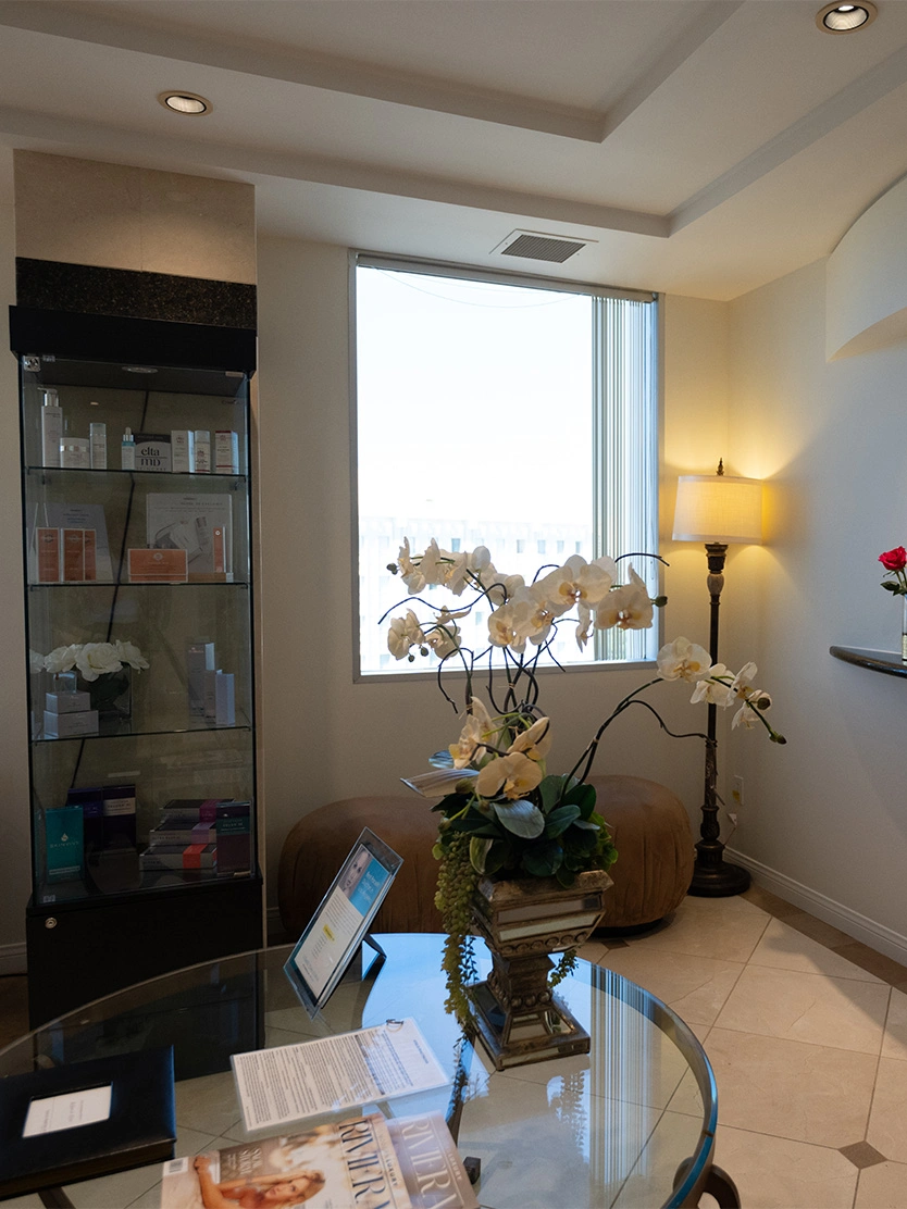 Elegant living room with glass coffee table, orchid centerpiece, floor lamp, and natural light from window - Skin care in Newport Beach, CA
