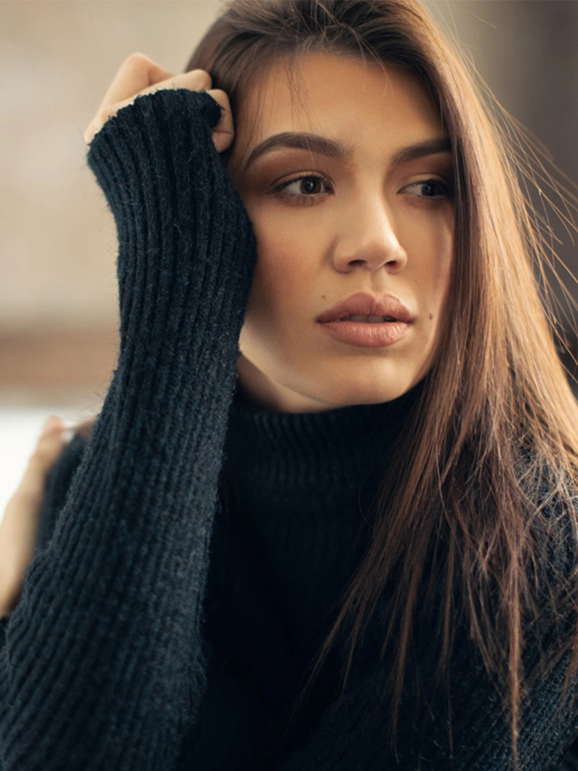 Woman in black turtleneck sweater with long brown hair resting hand on head in natural indoor lighting - Upper lip lift in Newport Beach, CA