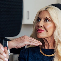 Mature woman with blonde hair examining her face while looking up, discussing facial rejuvenation procedure with doctor - Deep plane facelift in Newport Beach, CA