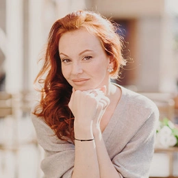 Red-haired woman with smooth facial features resting chin on hand showcasing natural beauty and youthful appearance - Facelift after weight loss in Newport Beach, CA