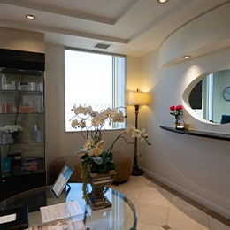 Modern medical spa reception area with orchid plant, glass table, and bright natural lighting from window - Skincare in Newport Beach, CA