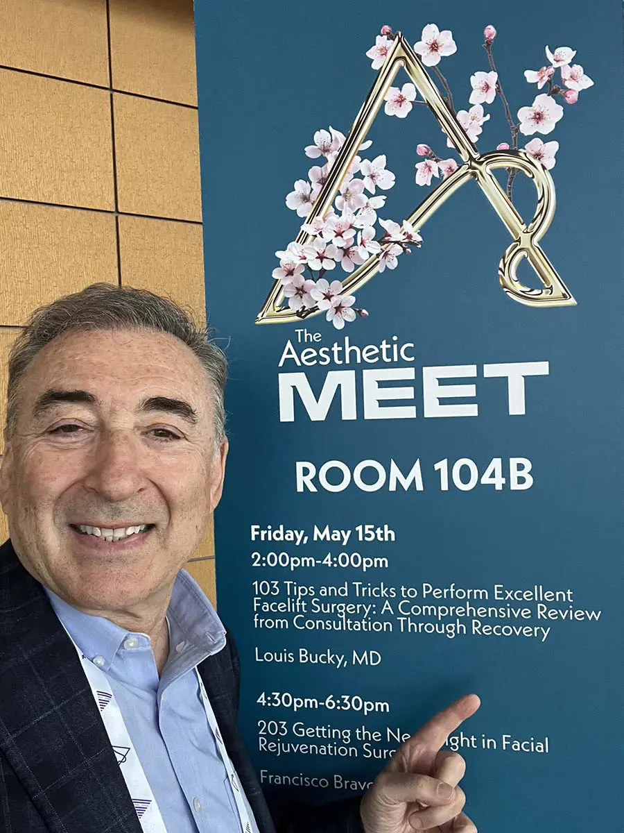 Boris M Ackerman MD posing with Aesthetic Meet event poster displaying cherry blossom logo and Room 104B details for Friday May 15th