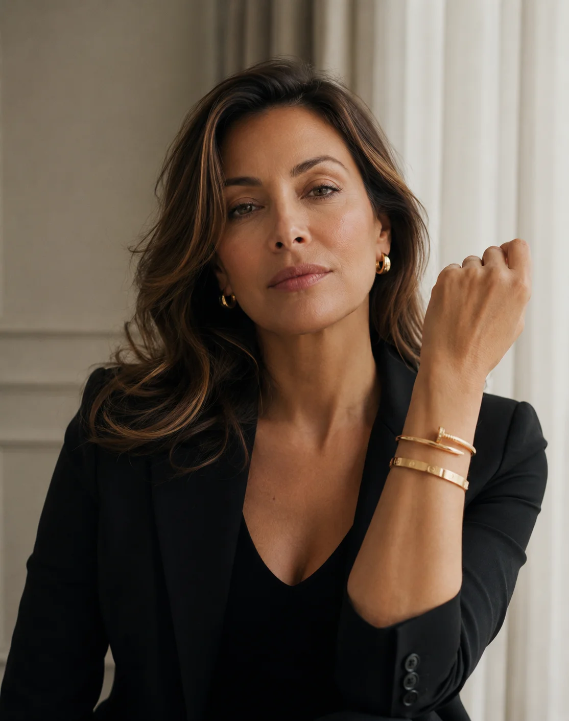 Woman in black blazer with gold bracelets posing elegantly in modern interior with neutral tones - Facelift in Newport Beach, CA