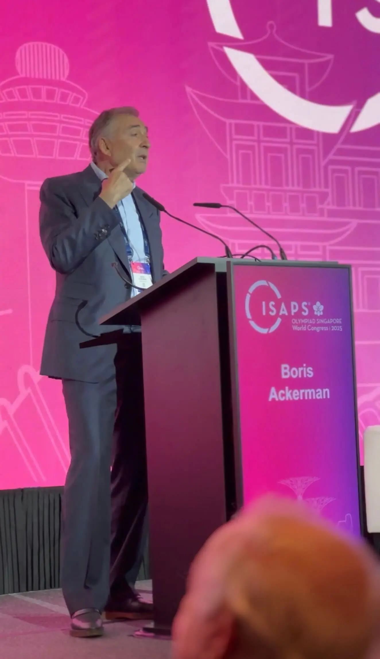 Dr Boris M Ackerman MD presenting at pink-themed conference podium with projection screen showing event branding