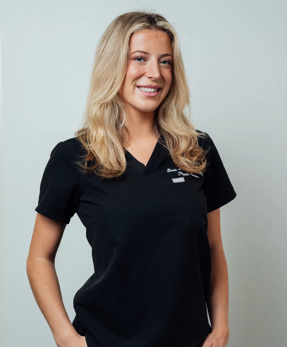 Smiling blonde woman wearing black polo shirt against gray background for staff profile